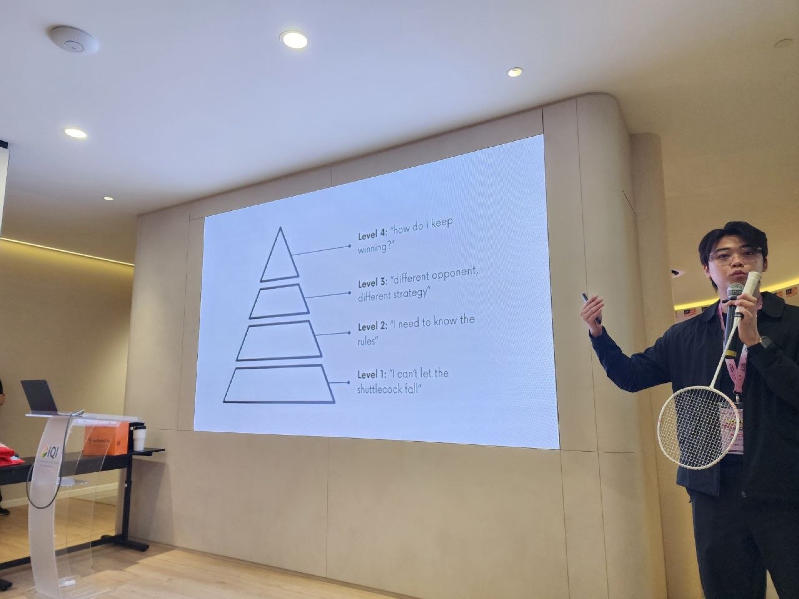 Bryan Low holding a badminton racket while presenting the four-level mastery pyramid at Youth Connect 2026